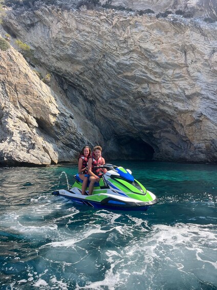 Two people on a jet ski in clear waters with rocky cliffs in the background. 4