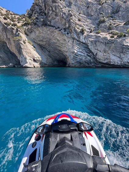 A jet ski moving through clear blue waters with rocky cliffs in the background. 2