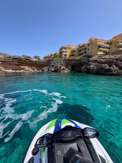 A jet ski on clear turquoise water with a rocky shoreline and yellow buildings in the background. 3