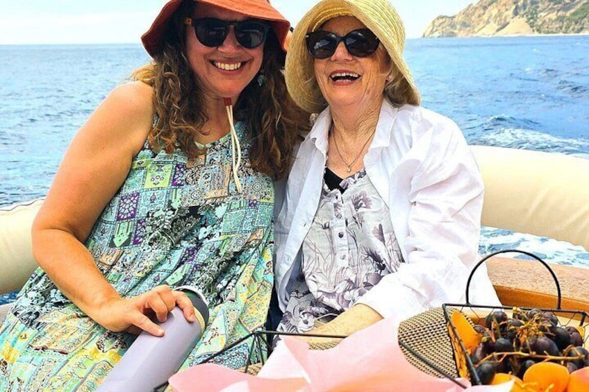Two people on a boat with a basket of fruits and a scenic coastal background. 5