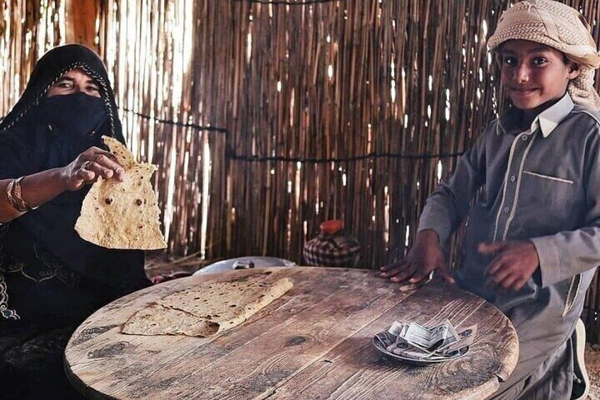 Two people sitting at a wooden table with flatbreads and a basket of bread. 4