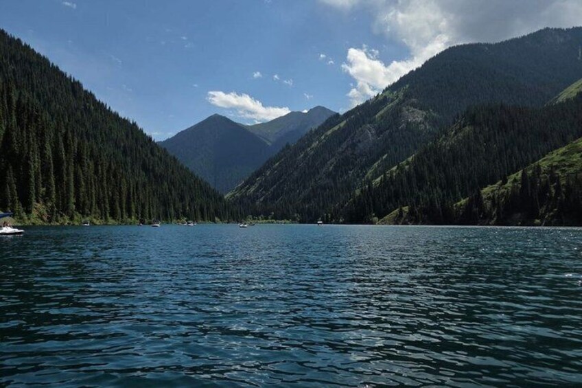 Ein ruhiger See, umgeben von bewaldeten Bergen unter blauem Himmel. 3