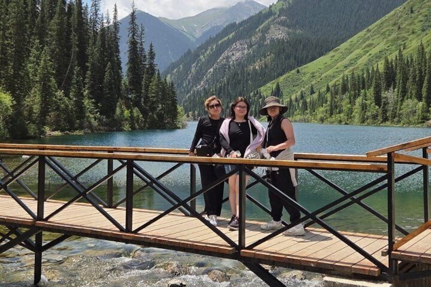 Eine Holzbrücke über einem See, im Hintergrund Berge. 2