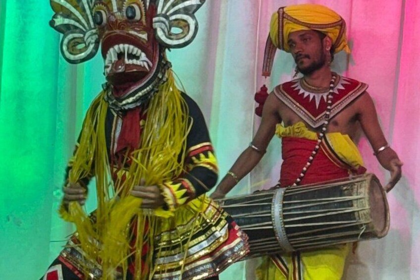 Two individuals in traditional attire, one with a mask and the other playing a drum. 2