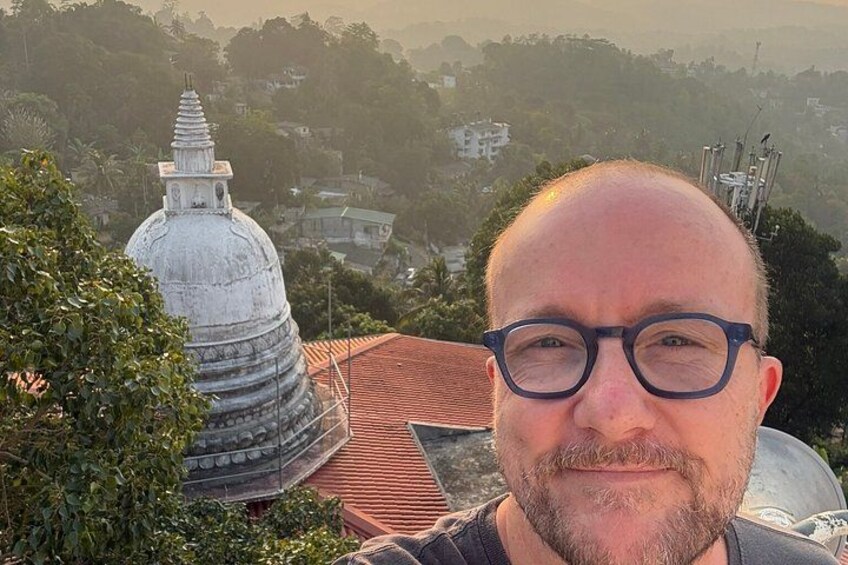 A person standing in front of a temple with a dome and a spire, surrounded by greenery and buildings in the background. 3