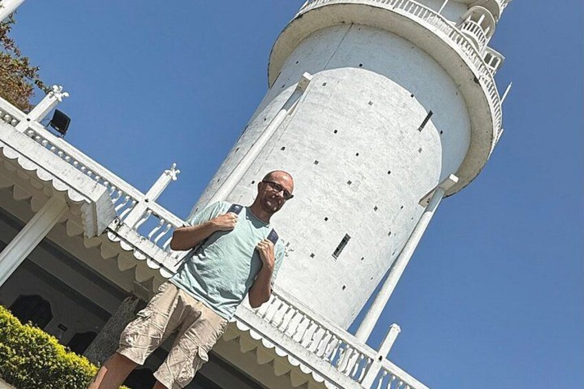 A person standing on a balcony with a lighthouse in the background. 5
