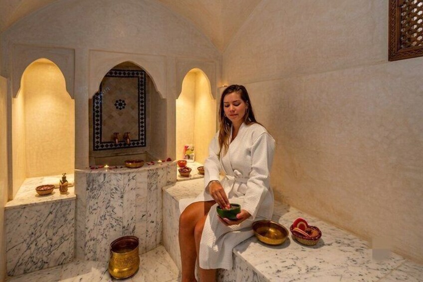 A person in a white robe sitting on a marble bench in a room with arches and a decorative wall. 2