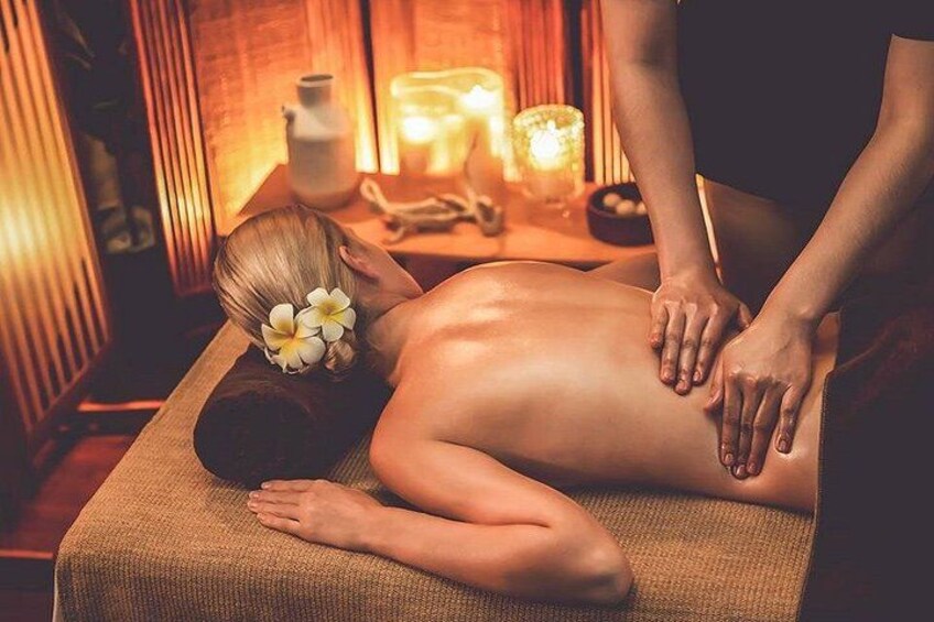 A person receiving a massage in a dimly lit room with candles and a wooden massage table. 4