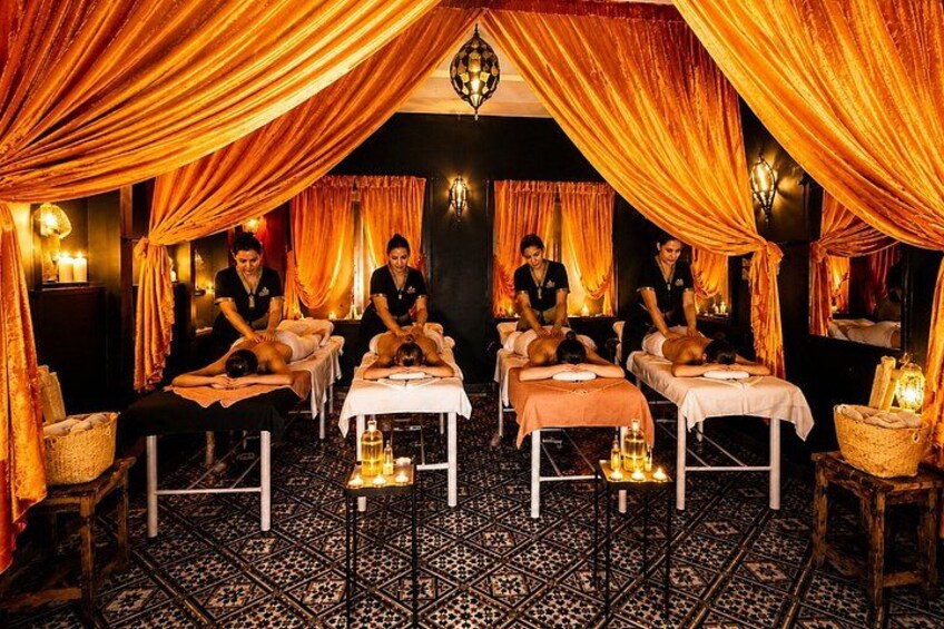 A traditional spa setting with draped curtains, massage tables, and attendants. 1