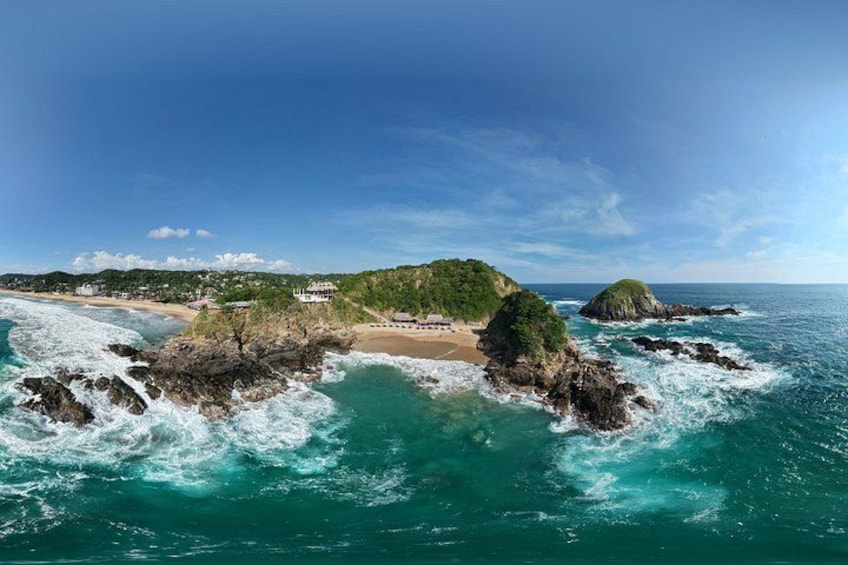 A coastal landscape with rocky formations, a beach, and a clear blue sky. 2