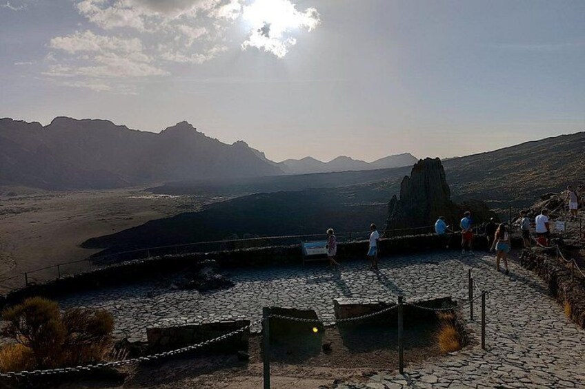 Paisaje rocoso con una gran formación rocosa, un sendero pavimentado y visitantes. 4