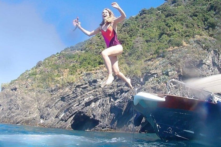Una persona saltando desde un acantilado rocoso al mar, con un bote cerca. 3