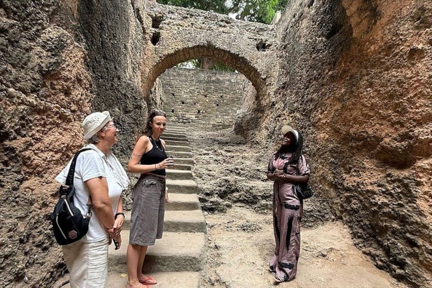 Three people standing on a stone pathway with a stone archway in the background. 5