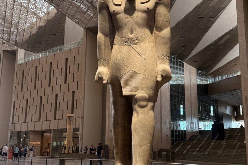 A large ancient Egyptian statue in a modern museum with a geometric patterned wall and stairs in the background. 4