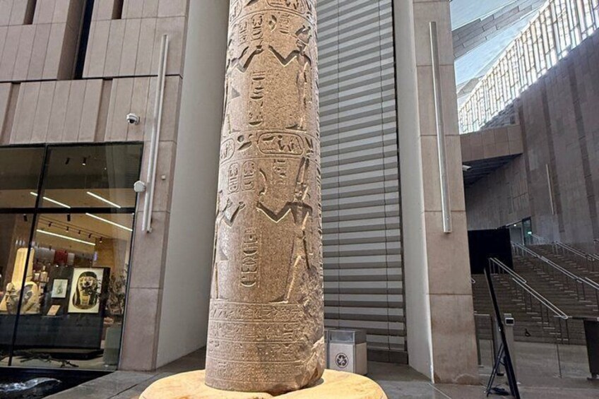 A large stone column with hieroglyphs, a modern building entrance, and a staircase. 2
