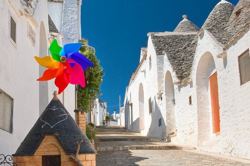 A narrow street lined with white buildings, a colorful pinwheel, and a clear blue sky. 2