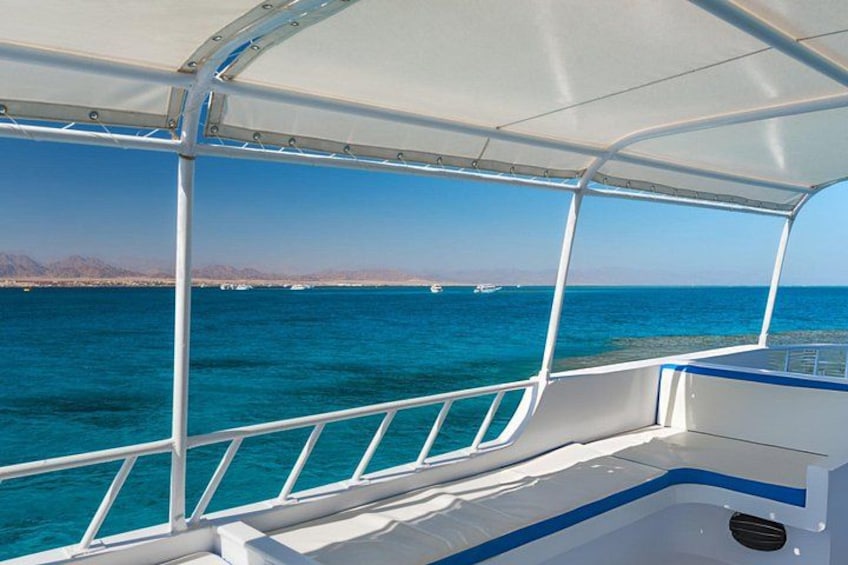 Un bateau surmonté d’un auvent blanc, une eau d’un bleu limpide et une terre lointaine à l’horizon. 4