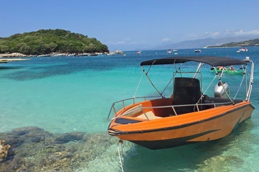 Una piccola barca arancione con una copertura nera su un mare turchese cristallino, con un'isola verde e una costa rocciosa sullo sfondo. 4