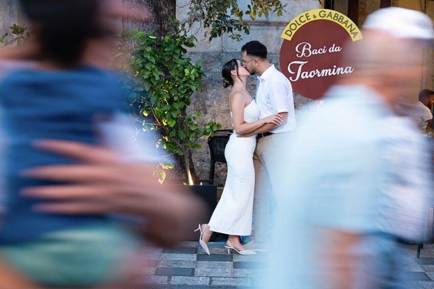 Una pareja abrazándose frente a un cartel que dice 'Dolce & Gabbana Baci da Tarmina'. 1