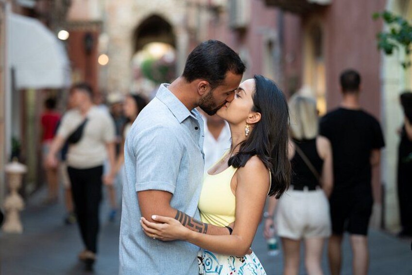 Una pareja abrazándose en una calle estrecha, con gente caminando al fondo. 4