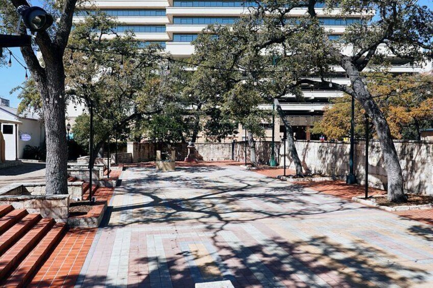 A paved pathway with trees, a building in the background, and a stone wall. 3