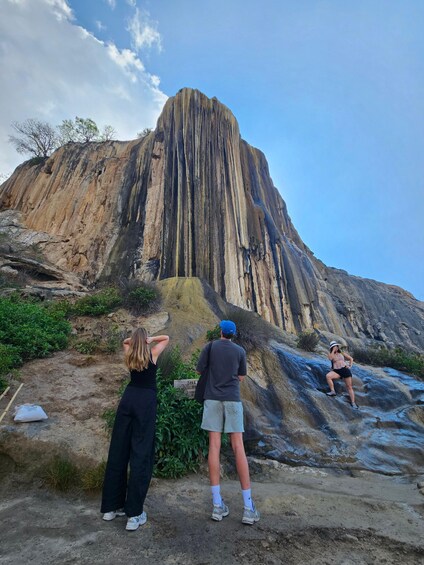 Three people standing on a rocky terrain with a large rock formation in the background. 3