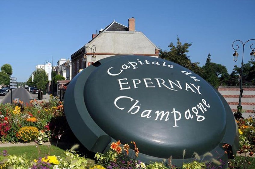Un grand panneau vert sur lequel on peut lire « Capitale d’Épernay, pays du Champagne », entouré de fleurs colorées et avec un bâtiment en arrière-plan. 4