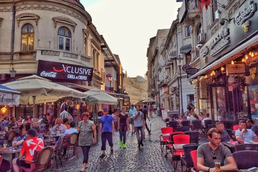 Una strada acciottolata fiancheggiata da caffè e ristoranti con tavoli all'aperto, e persone che passeggiano e siedono. 5