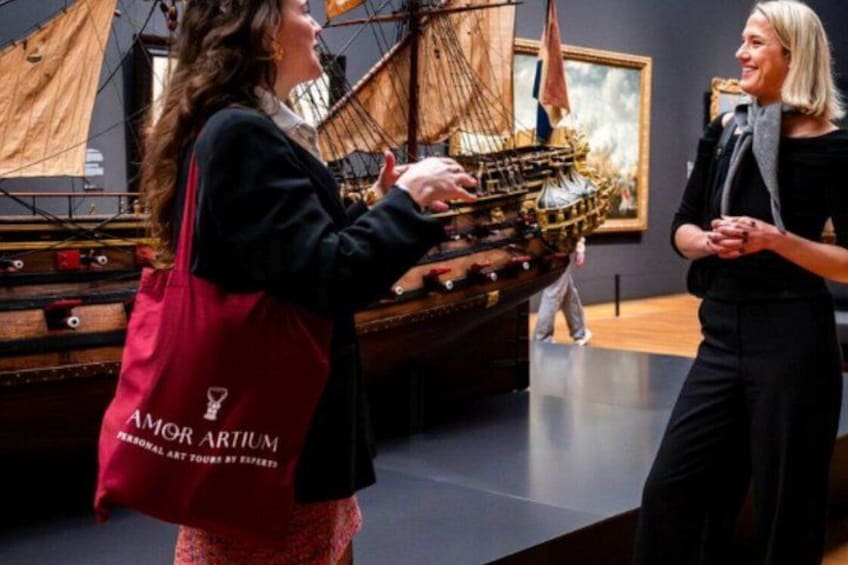 Iemand houdt een modelboot vast in een museum, met tentoonstellingen op de achtergrond. 1