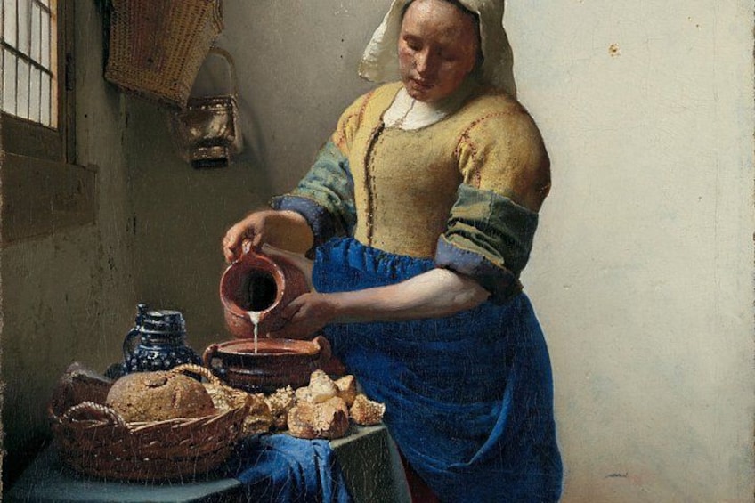 Een vrouw giet melk in een kom, omringd door brood en aardewerk op een tafel. 2