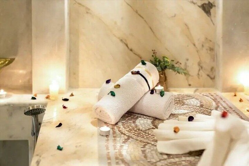A marble-topped bathroom with towels, candles, and a decorative vase. 5