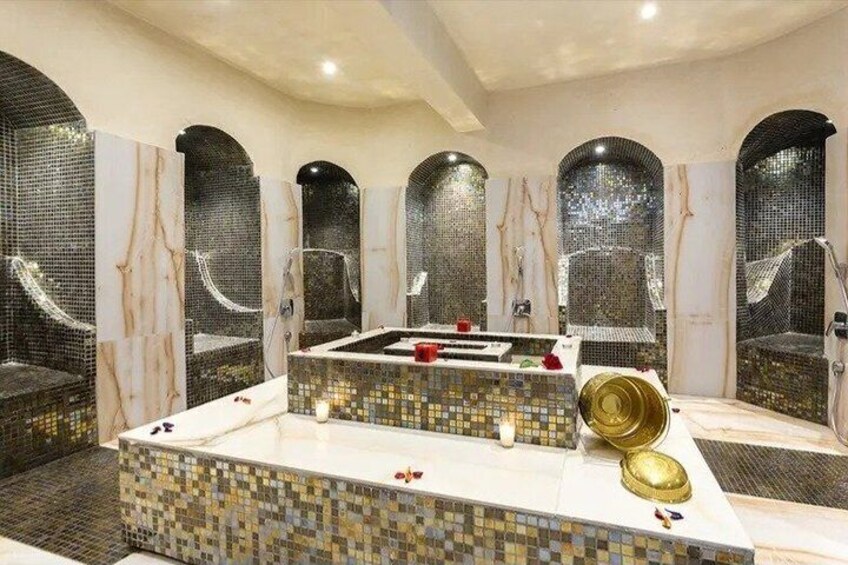 A luxurious bathroom with mosaic walls, a central bathtub, and multiple shower areas. 1