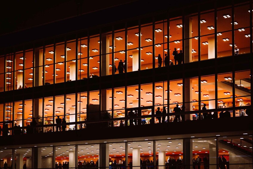 A multi-level building with illuminated interiors and people on the balconies. 3