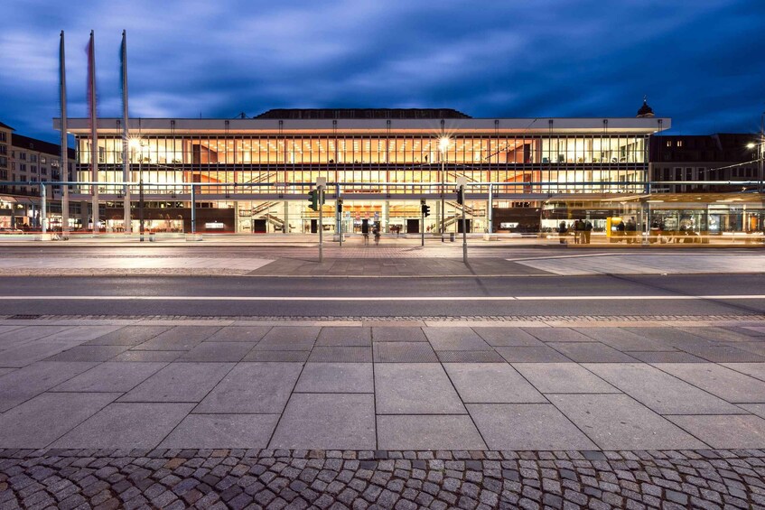 A modern building with a glass facade and a dome on top, situated at a city intersection with a cobblestone plaza in front. 2