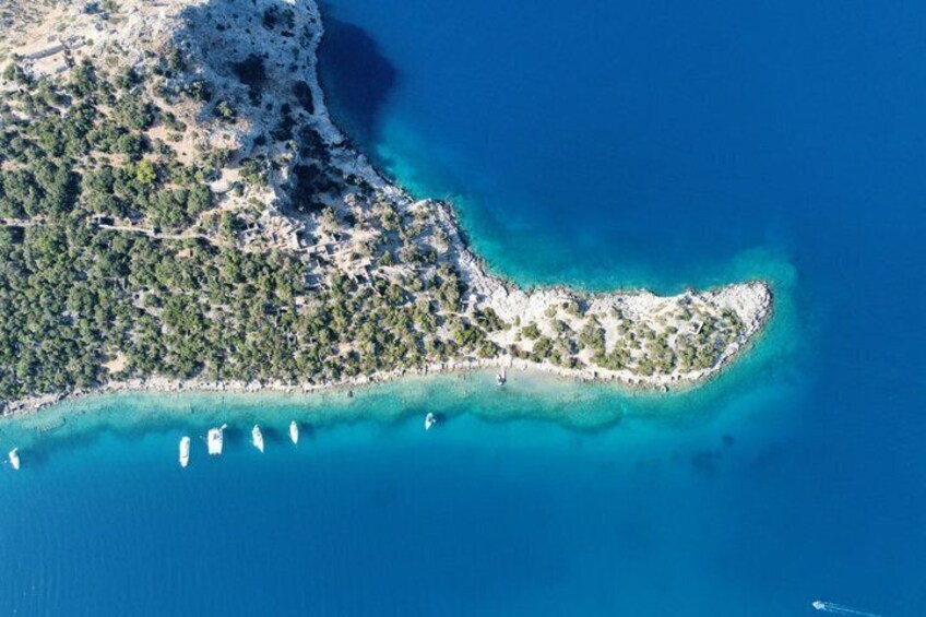 Una vista aerea di un’isola costiera con acque turchesi cristalline, una spiaggia sabbiosa e diverse imbarcazioni ancorate al largo. 2