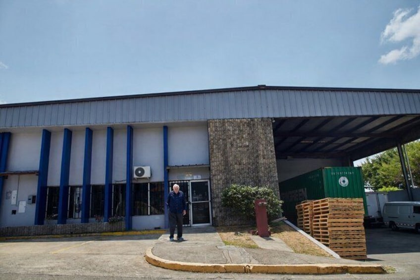A building with a covered entrance, blue vertical columns, and a stack of wooden pallets. 1