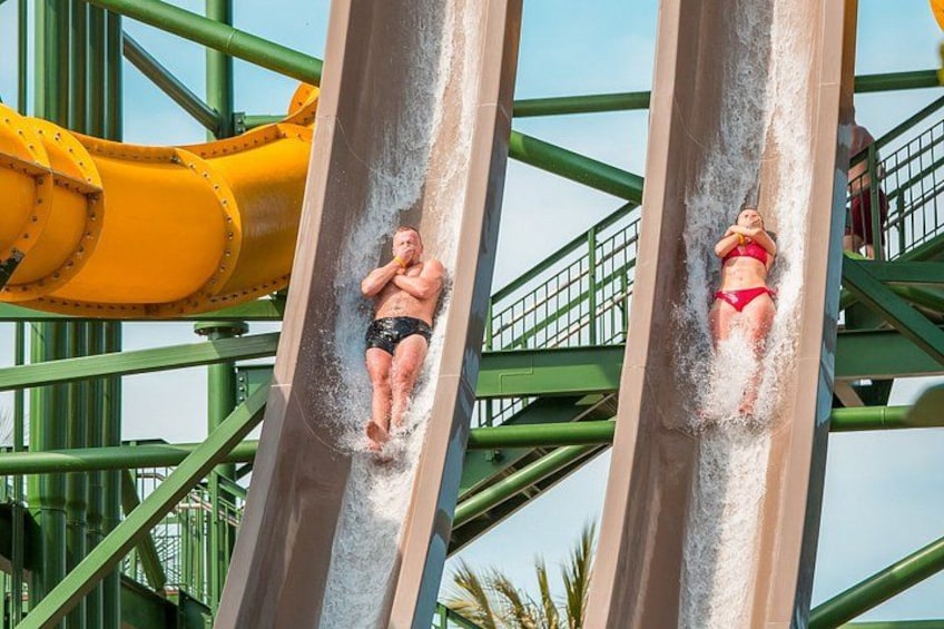 Zwei Personen rutschen eine Wasserrutsche hinunter, im Hintergrund eine gelbe Struktur. 2