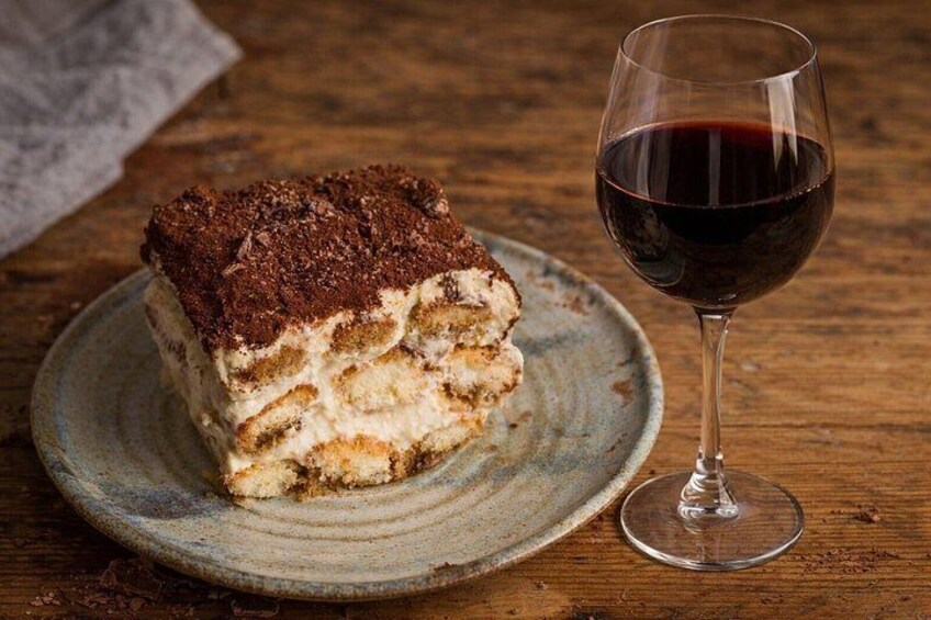 A slice of tiramisu on a ceramic plate with a glass of red wine. 3