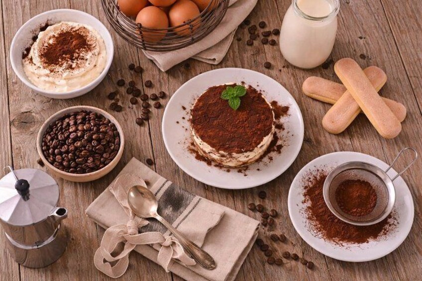 Une table en bois dressée pour le dessert, avec un tiramisu, des grains de café, des biscuits secs et un moulin à café. 1
