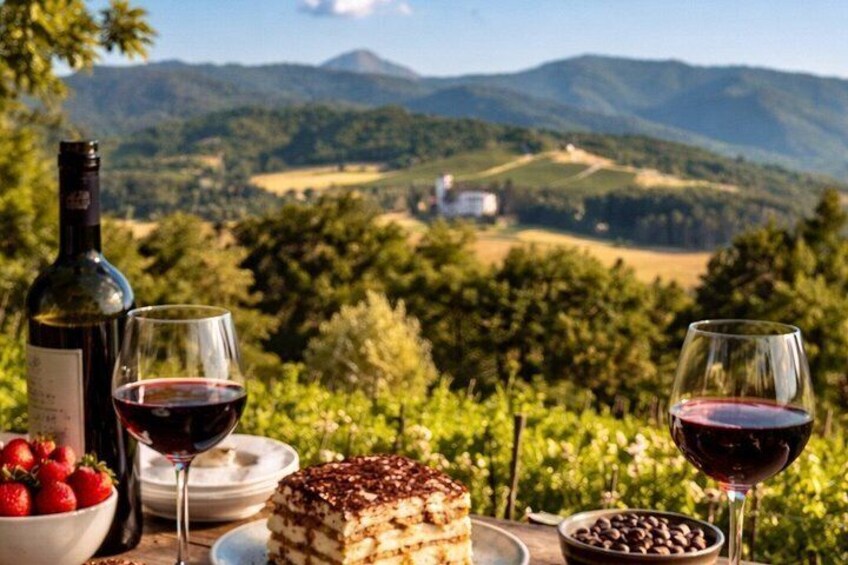 A vineyard with a table set for a meal, including a bottle of wine, glasses, strawberries, a dessert, and chocolate. 2