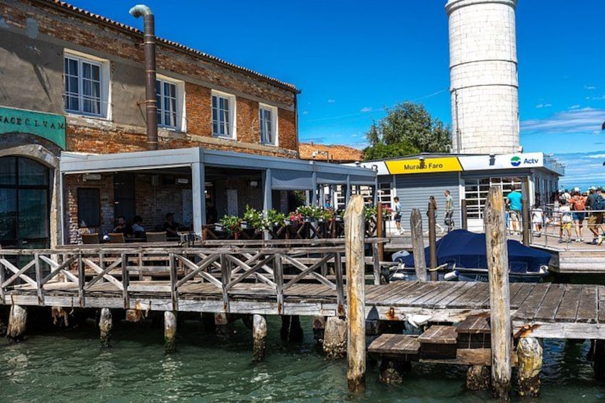 A wooden dock extending into a body of water, a brick building with a sign, and a white cylindrical structure in the background. 2
