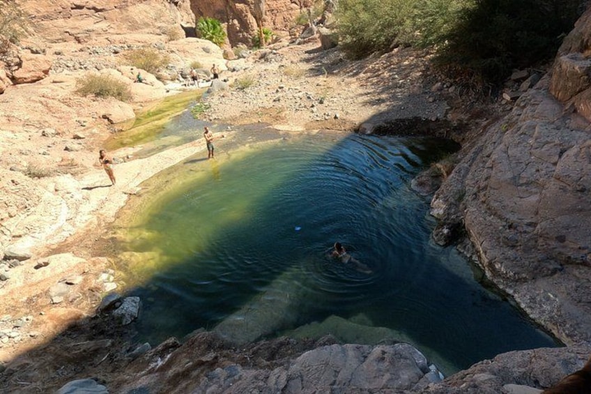 Una piscina naturale circondata da un paesaggio roccioso, con persone che nuotano e si fermano nelle vicinanze. 4