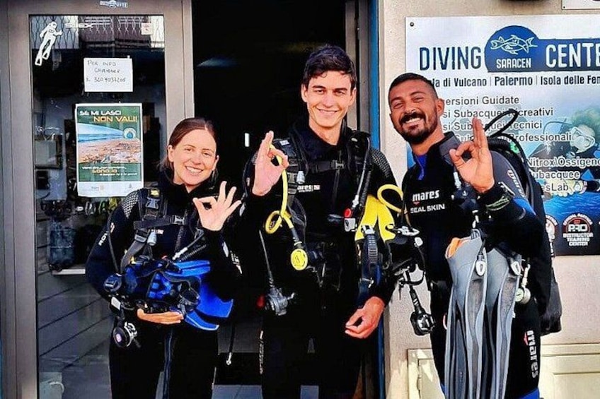 Tres personas con equipo de buceo frente a un centro de buceo. 3