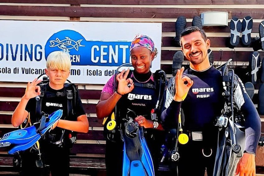 Tres personas sosteniendo equipo de buceo frente a un letrero que dice 'DIVING CENTRO'. 5