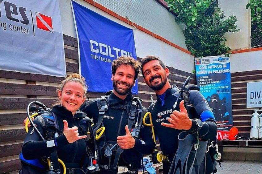 Tres personas con equipo de buceo posando frente a un centro de buceo. 1
