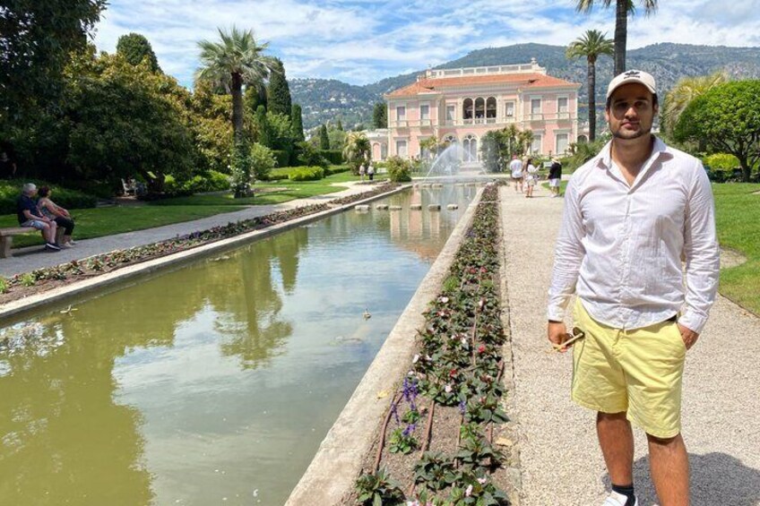 A man standing by a calm waterway with a building in the background. 1