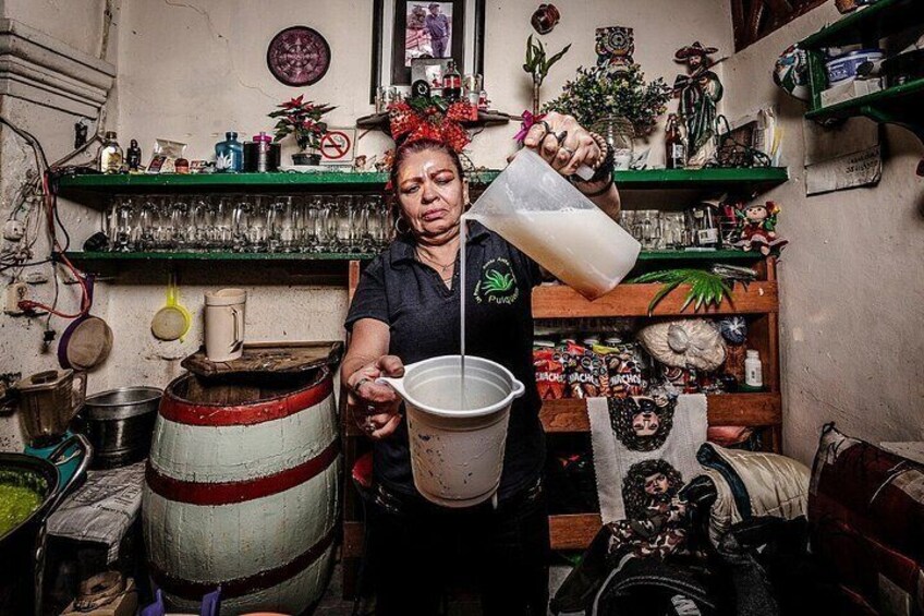 Une personne verse un liquide d’une cruche dans un seau, dans une pièce encombrée où se trouvent des étagères et divers objets. 4