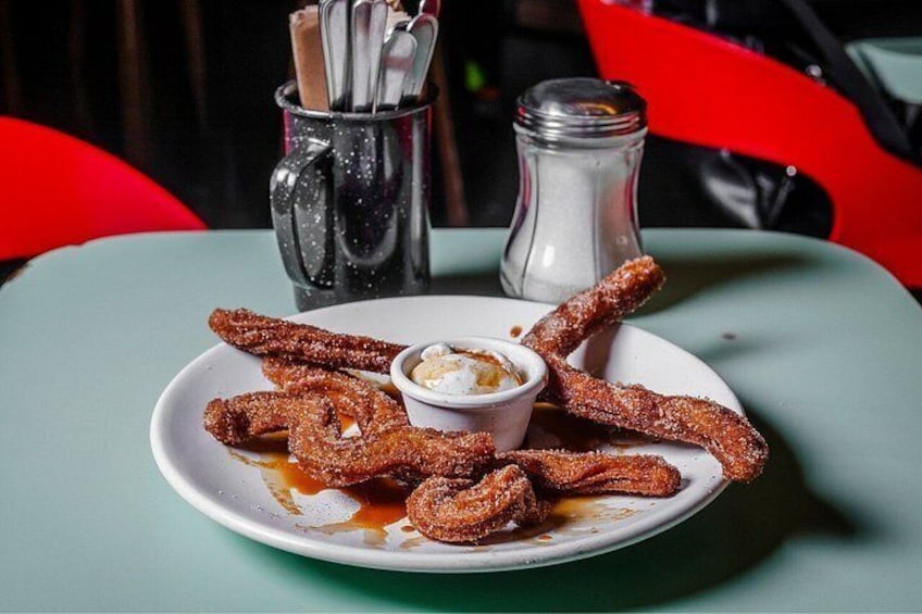 Une assiette de churros accompagnée d’une sauce pour tremper, d’un salier et d’un sucrier, le tout posé sur une table. 2