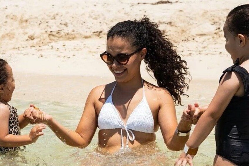 Une personne vêtue d’un bikini blanc, tenant la main de deux autres personnes sur une plage de sable. 4