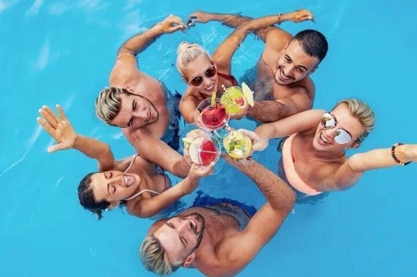 A group of people in a swimming pool, holding drinks. 1